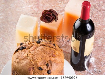 Delicious whole panettone, Christmas cake with glass, bottle of wine, candles, dried red rose set on marble table.