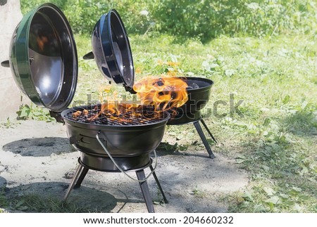 Flames buring in portable BBQ grills visible at picnic summer camp.