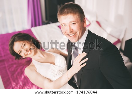 laughing bride and groom in sunny bedroom