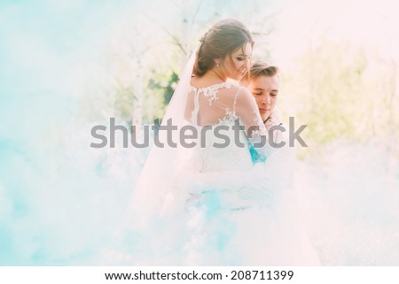 groom embracing bride in turquoise smoke on nature