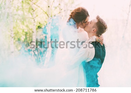 bride kissing groom in turquoise smoke on nature