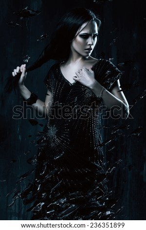 woman in black dress holding hair with broken glass in dark