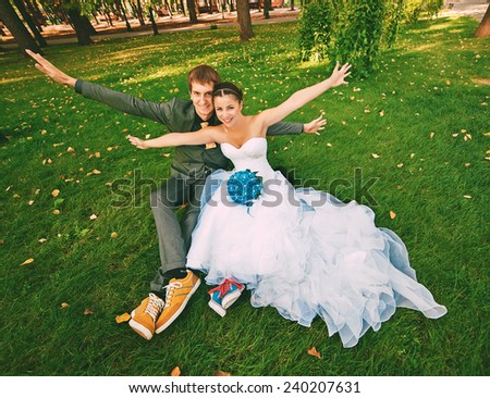 funny groom and bride sitting on grass in park