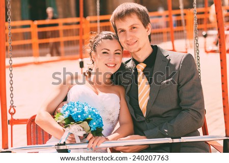 smiling bride and groom on merry-go-round at sunny day