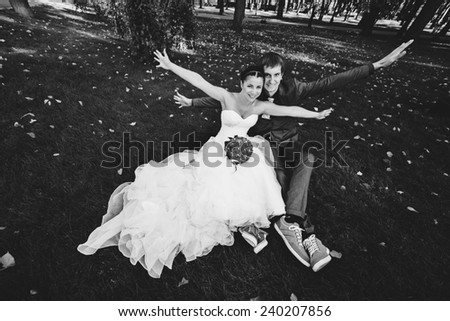 black and white funny groom and bride sitting on grass in park