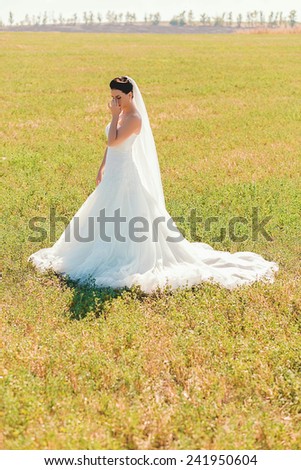 sensual bride in long white dress on field in sunlight