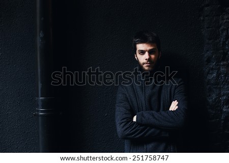 serious man in coat near black wall in the evening