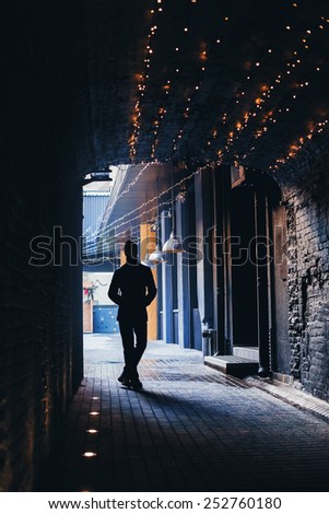 silhouette of man in dark tunnel with yellow lights