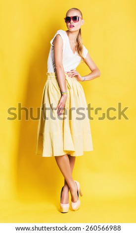 blond woman in yellow skirt and pink sunglasses on yellow background