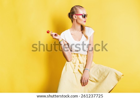 sexy beautiful woman in skirt and sunglasses with lollipop on yellow background