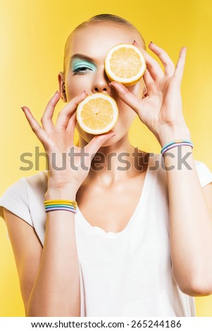 attractive woman with lemon near eye on yellow background