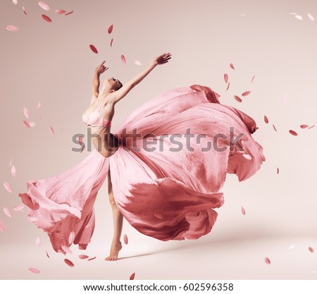 ballerina dancing in flowing pink dress with flying petals in studio