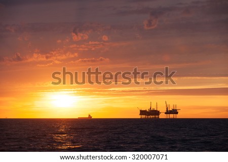 Silhouette of an offshore oil platform and supply vessel at sunset