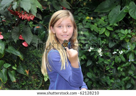 Young girl holding butterfly on her hand as she looks at camera and gives a shy smile in the forest.