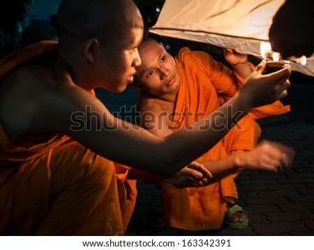 Chiang Mai, Thailand - November 17, 2013: Two orange-robed Buddhist monks lighting up hot air balloon during Loy Krathong festival in Chiang Mai, Thailand.