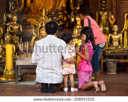 Ayutthaya, Thailand - March 2, 2014: Unidentified Asian Buddhist family praying and making offerings in front of Buddhist shrine at ancient temple in Thailand\'s former capital, Ayutthaya.