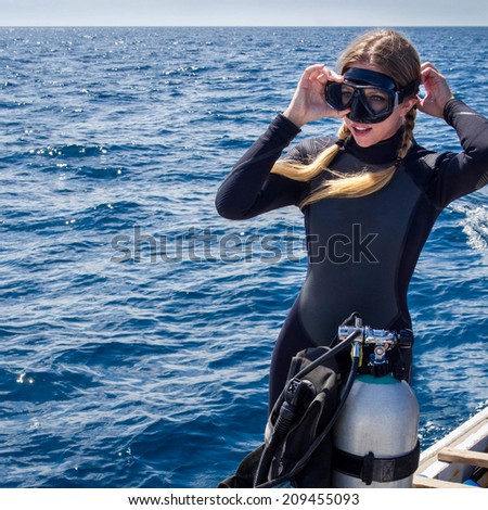 Beautiful, Caucasian diver on a boat in the ocean putting on goggles in preparation for scuba diving.