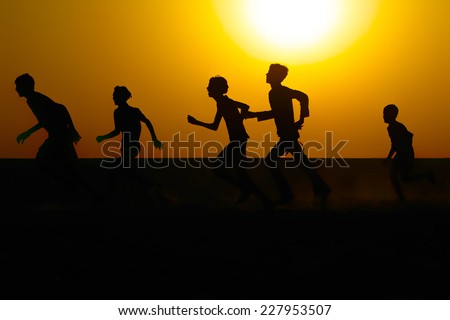 Silhouette of boys running in a field against a warm sunrise sky.
