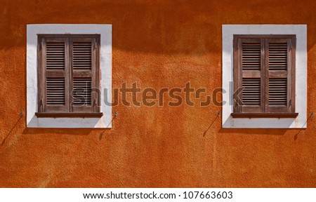 Orange wall of the house with a window with brown shutters in a midday sun ,Menorca, Balearic Islands, Spain