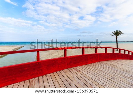 Red wooden footbridge sand beach sea white clouds blue sky palm tree, Alcudia, Majorca island, Spain