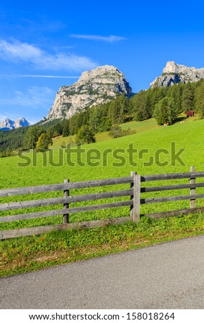 Green alpine pasture wooden fence road view, La Villa village, Dolomiti Mountains, Italy
