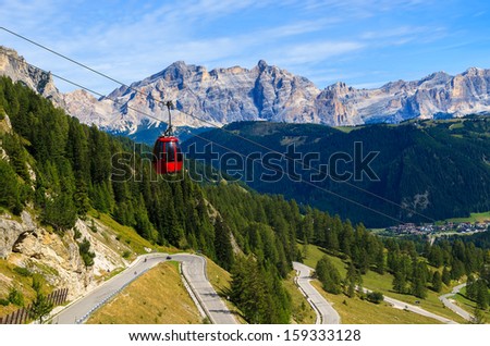 Red gondola car lift twisting road to Passo Gardena from Colfosco village, Dolomites Mountains, Italy