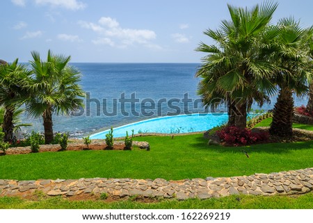 Path in green grass area with palm trees swimming pool at east coast of Atlantic Ocean, Madeira island, Portugal
