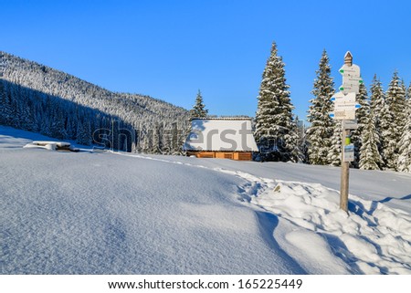 Direction signs on winter trail and mountain hut covered with fresh snow on Rusinowa Polana in High Tatra Mountains, Poland