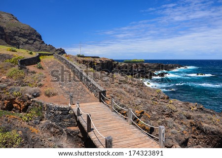 Wooden bridge on walking promenade along ocean on northern coast of Tenerife island with Teno mountains in the background, Canary island, Spain