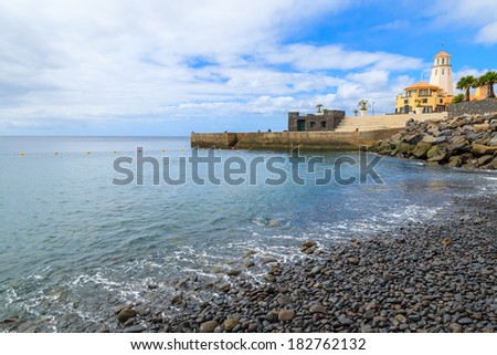 Black volcanic stones on beach with lighthouse in the background, Madeira island, Portugal