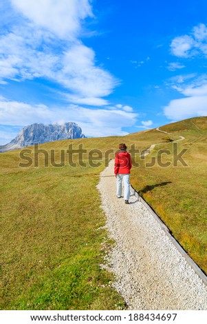 Young woman walking on path with Sassolungo mountain range view near Passo Gardena in autumn, Dolomites Mountains, Italy