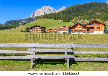 Wooden bench and pasture fence in alpine La VIlla village with houses and Dolomites Mountains in the background, Italy