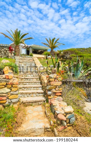 Stone walkway to holiday house on coast of Sardinia island seen from coastal path, Italy