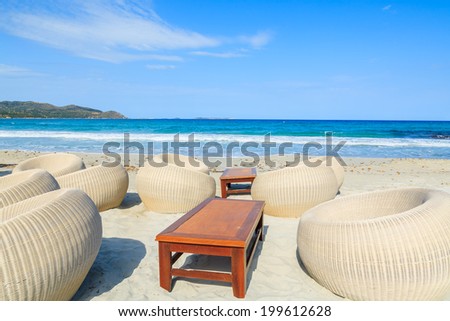 Chairs in a beach bar with wooden table on white sand in Porto Giunco bay, Sardinia island, Italy