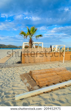 Fence and palm tree on sandy Porto Giunco beach in warm sunset light, Villasimius, Sardinia island, Italy
