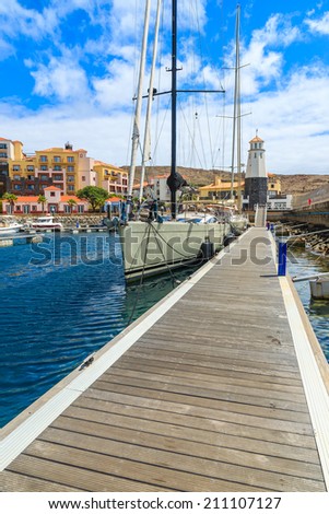 Luxury yacht anchors at wooden pier in marina with colorful houses of Portuguese village in background, Madeira island, Portugal
