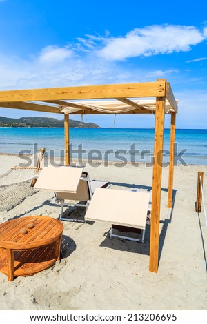 Sunchairs with wooden teak table on white sand beach in Porto Giunco bay, Sardinia island, Italy