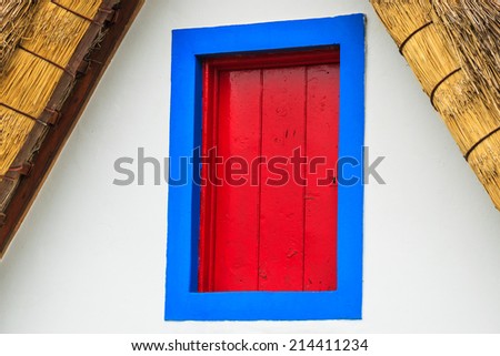 Blue window frame and red shutters of traditional thatched house in Santana village, Madeira island, Portugal
