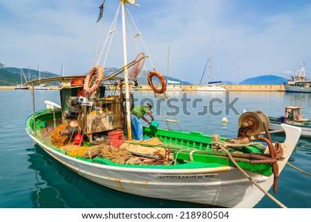 SAMI PORT, KEFALONIA ISLAND, GREECE - SEP 20, 2014: fisherman cleans traditional greek fishing boat in port of Sami village. Colorful boats are symbol of Greek islands.