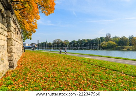Couple of unidentified people riding bikes along a Vistula river in Krakow on sunny autumn day. Krakow is most visited city in Poland among foreign tourists.