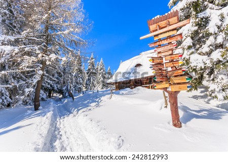Trail sign with directions and wooden mountain hut on path in snow to Turbacz in winter landscape of Gorce Mountains, Poland