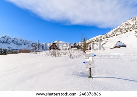 Mountain trail sign buried in snow in Gasienicowa valley with huts in distance, Tatra Mountains, Poland