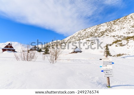 Mountain trail sign buried in snow in Gasienicowa valley with huts in distance, Tatra Mountains, Poland