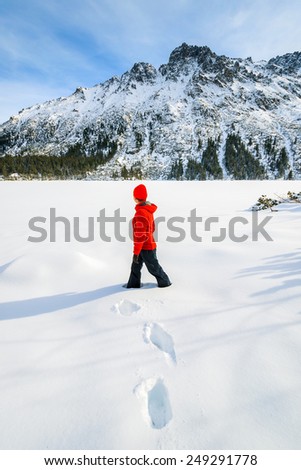 Young woman tourist in red jacket standing in deep fresh snow on frozen Morskie Oko lake in winter, Tatra Mountains, Poland
