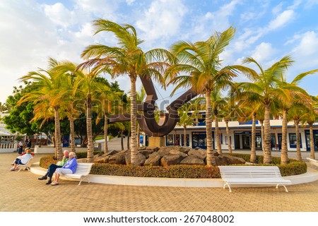 PUERTO CALERO MARINA, LANZAROTE ISLAND - JAN 12, 2015: square with palm trees and people sitting on bench in Puerto Calero port built in Caribbean style. This is a modern yacht marina.
