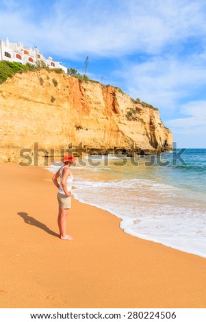 Young woman tourist standing on Carvoeiro beach with turquoise sea water and cliffs, Portugal