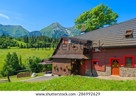 Typical wooden house on green meadow with Tatry Bielskie Mountains in background in summer, Slovakia