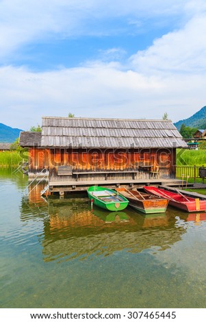 Three colorful fishing boats and wooden cabin on shore of Weissensee lake in summer landscape of Carinthia land, Austria