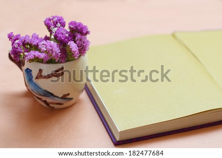 Purple flowers in a vase and book on the wooden table