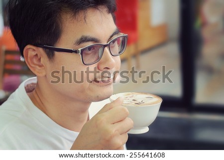 Asian man wearing glasses drinking coffee in coffee shop,retro and vintage tone